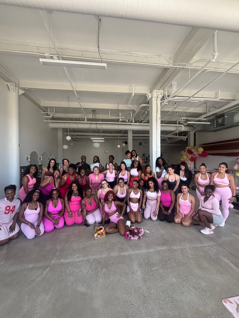Community gathering in pink athletic wear with flowers and balloons